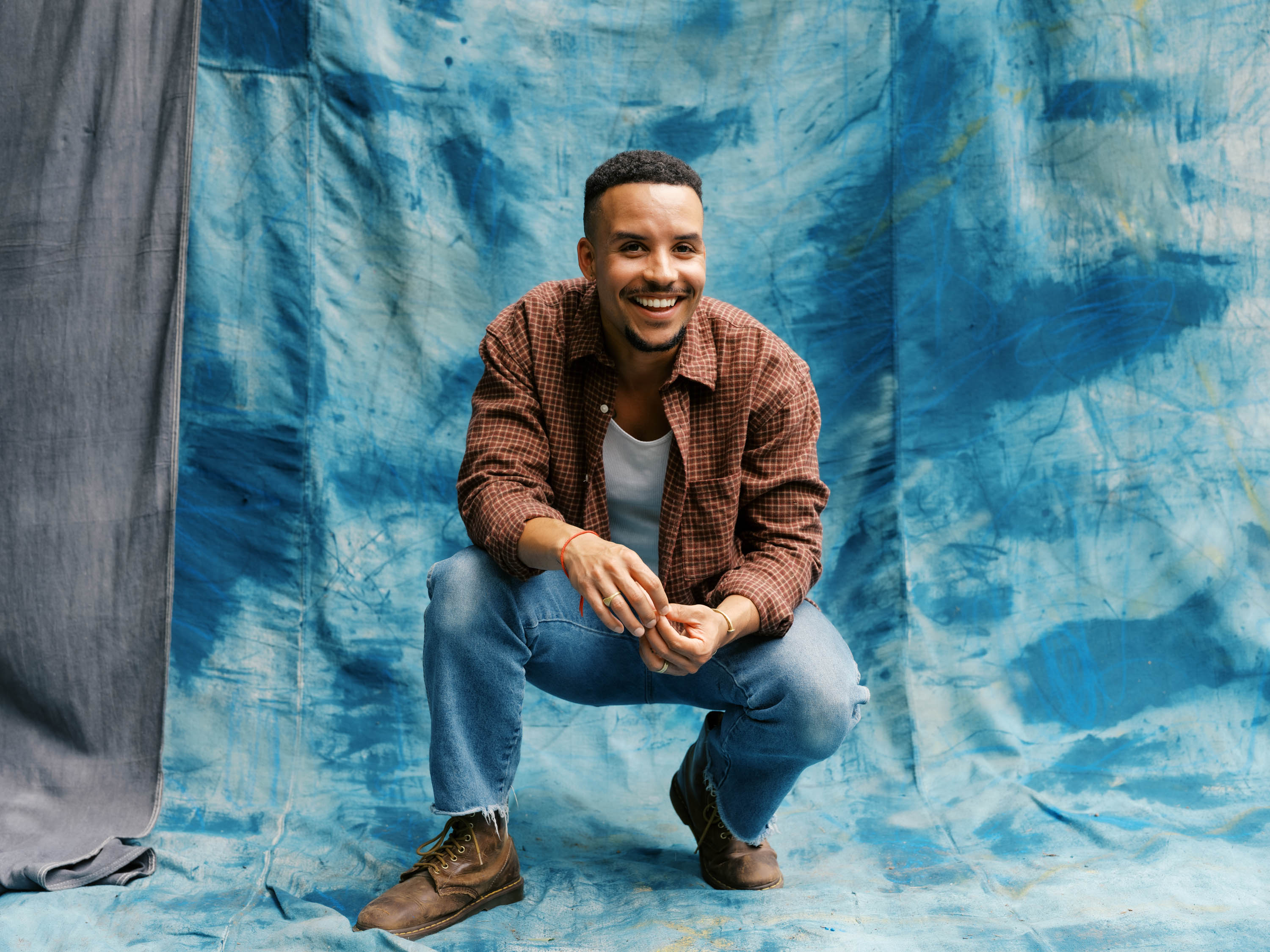 Tavior Mowry crouching and smiling against a blue painted backdrop